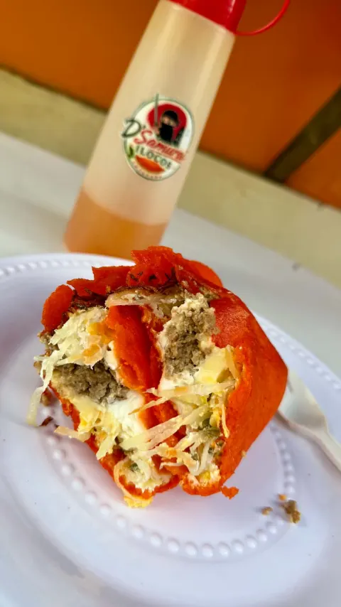 An empanada cut open on a plate, showing egg, papaya and longganisa, with a bottle of D'Samurai suka behind it