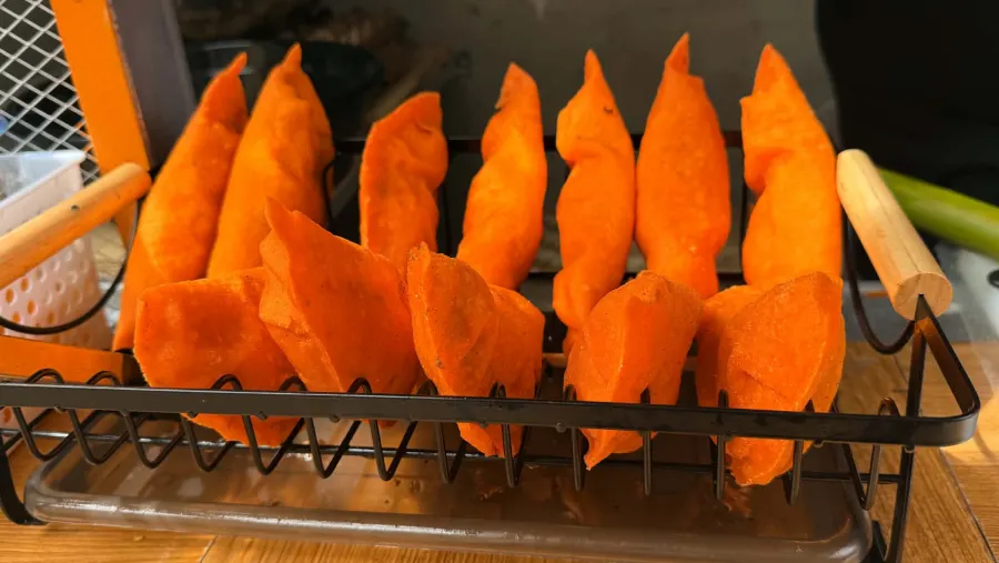 Freshly fried empanadas standing in a draining rack next to the fryer